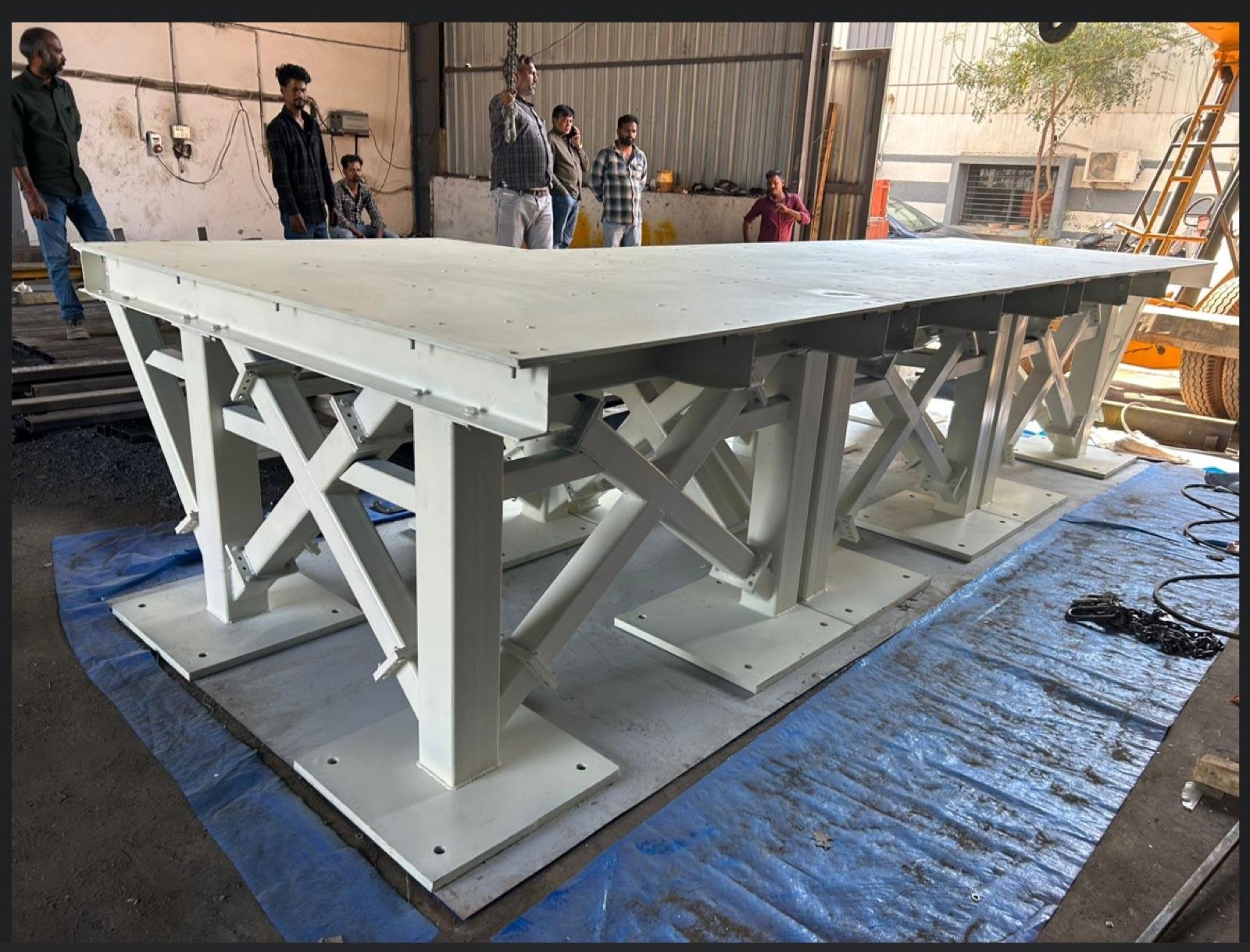 Large fabricated steel platform structure with cross-braced legs, painted and set on the workshop floor