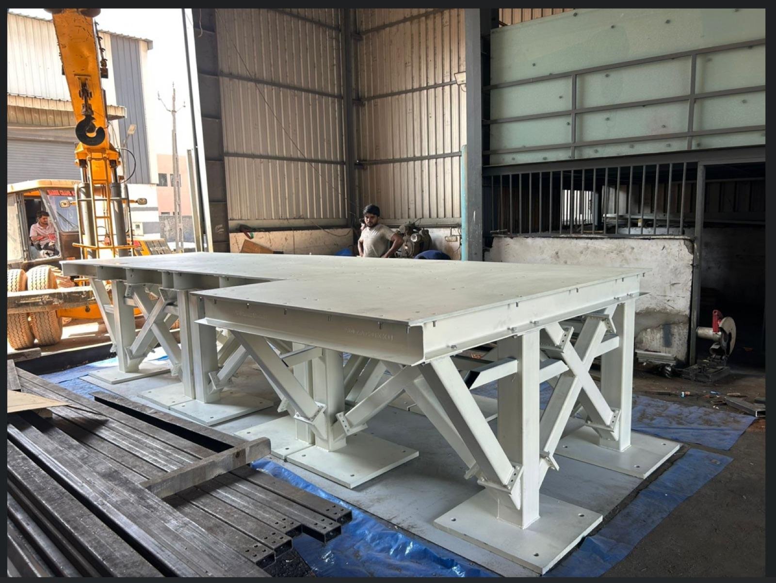 Two white-painted heavy fabricated steel platforms on support columns inside the Zensteel Works workshop, with an orange mobile crane alongside